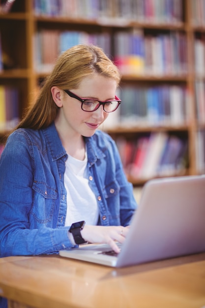 Studente con smartwatch usando il portatile in biblioteca