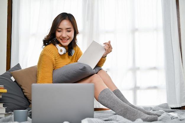 Studente di college femminile asiatica attraente che fa i compiti lavorando al suo progetto sul computer portatile