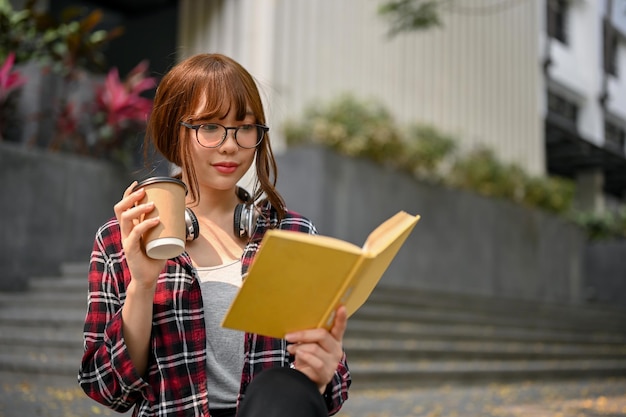 Studente di college femminile asiatico intelligente che si concentra sulla lettura di un libro mentre si siede sulle scale