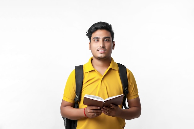 Studente di college indiano in piedi con borsa e libro di lettura su sfondo bianco.