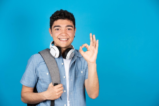 Studente di college ispanico che fa segno ok e sorride alla telecamera isolata su sfondo blu