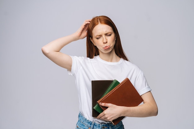 Studente di college triste dispiaciuto della giovane donna che tiene libro e che guarda l'obbiettivo su sfondo grigio