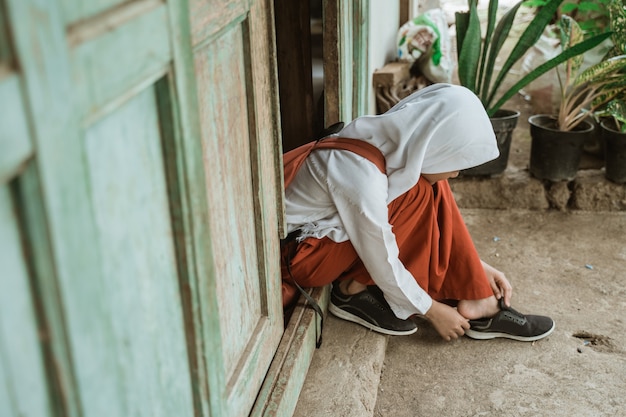 Studente di scuola elementare indonesiano si prepara a scuola la mattina allacciando le scarpe davanti alla casa