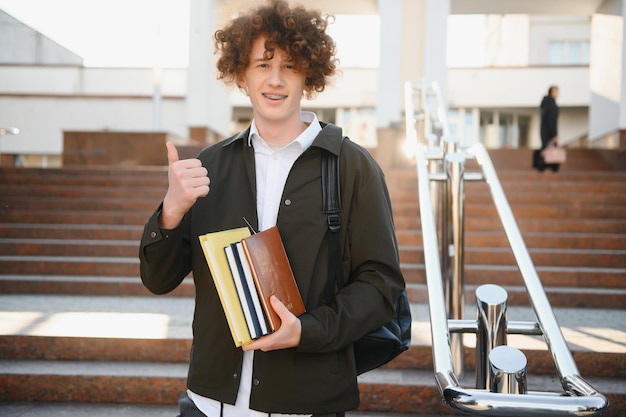 Studente eccitato che ha una pausa tra le classi vicino all'università che sorride alla telecamera all'aperto