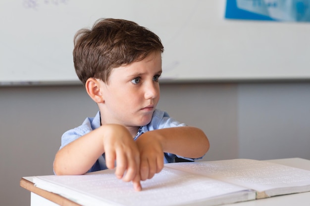 Studente elementare caucasico che indica il braille mentre studia alla scrivania in classe