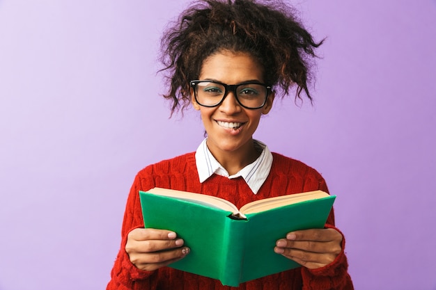 Studente felice afroamericano in tenuta uniforme e libro di lettura, isolato