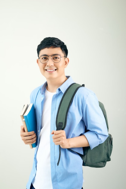 Studente felice bello sorridente e uno zaino e quaderni sul muro bianco