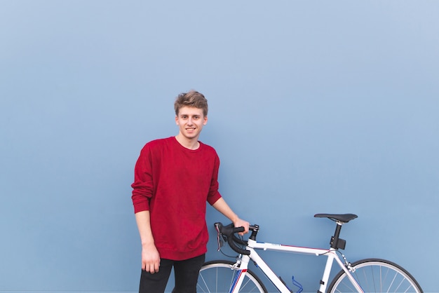 Studente felice che sta ad una bicicletta bianca su un fondo blu