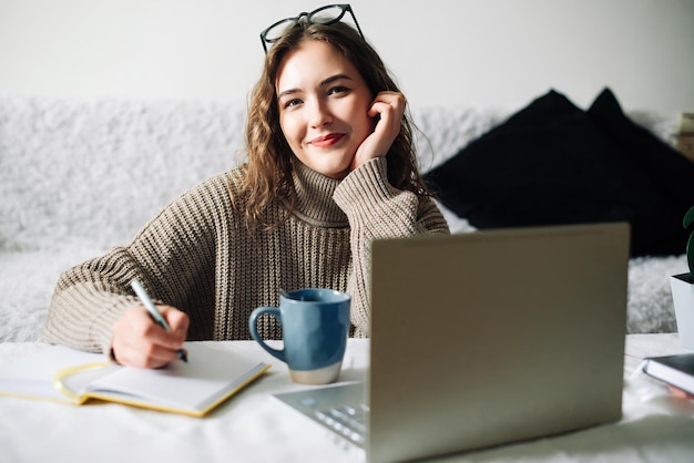 Studente felice che studia a casa facendo i compiti e preparandosi per gli esami davanti al laptop seduto a