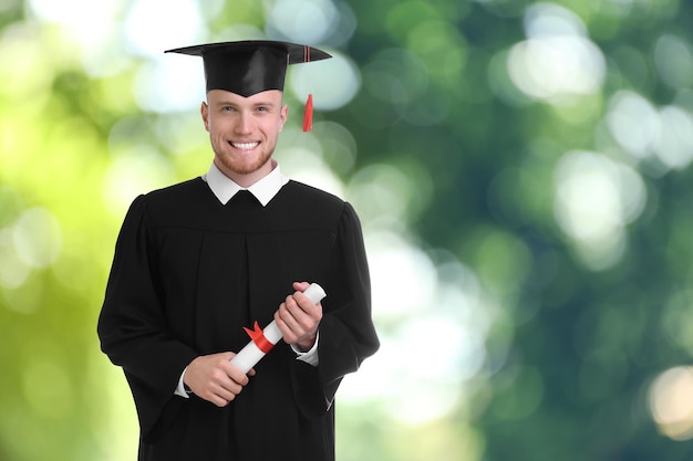 Studente felice con cappello di laurea e diploma sullo spazio di sfondo sfocato per il testo