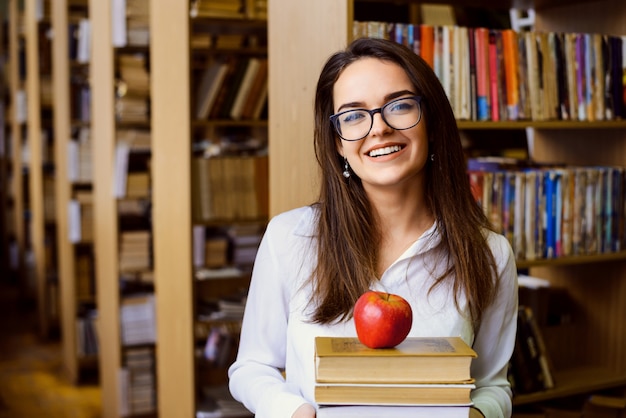 Studente felice con molti libri e una mela in biblioteca