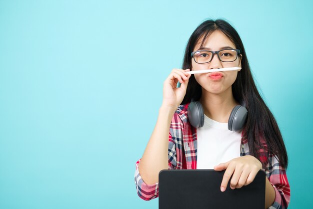 Studente felice. Ragazza asiatica allegra che sorride alla macchina fotografica che sta con lo zaino in studio sopra fondo blu. Torna al concetto di scuola.