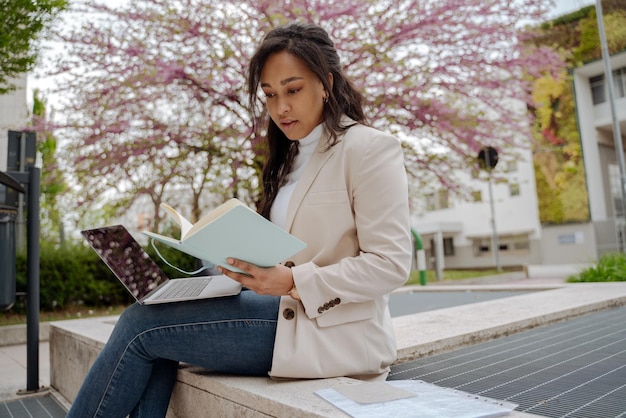 Studente fiducioso che studia libro di lettura seduto nel campus universitario, concetto di istruzione