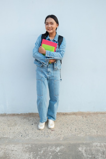 Studente giovane ragazza in piedi a scuola indossare jean tenere libro con sfondo zaino blu