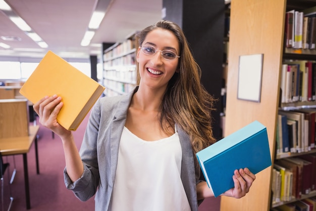 Studente grazioso che sorride alla macchina fotografica in biblioteca