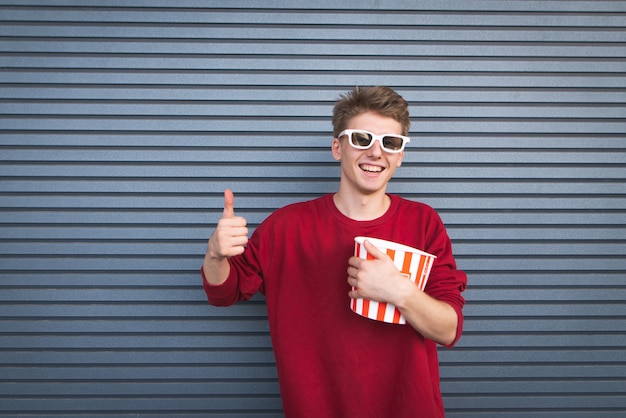 Studente in occhiali 3D e una tazza di popcorn in mano mostra un pollice in alto