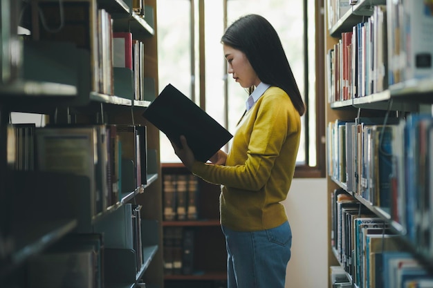 Studente in piedi e libro di lettura in biblioteca