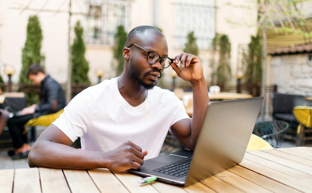 Studente intelligente africano che sfoglia gli articoli su Internet mentre è seduto al caffè all'aperto