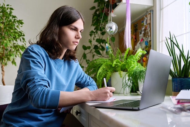 Studente maschio adolescente che studia a casa utilizzando un computer portatile