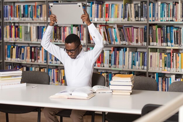 Studente maschio africano che lancia il computer portatile e vuole distruggerlo Profondità del campo poco profonda