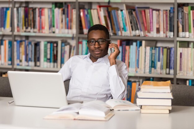 Studente maschio africano che parla al telefono nella profondità del campo poco profonda della biblioteca