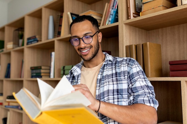 Studente maschio arabo che legge il libro e impara mentre si siede nella biblioteca universitaria all'interno dello spazio della copia