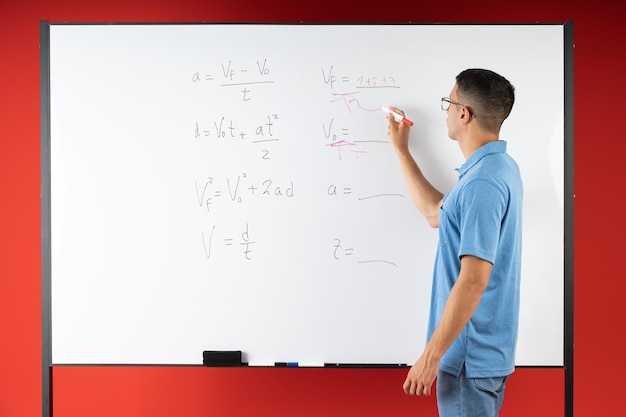 Studente maschio che fa esercizi di matematica sulla lavagna bianca con un pennarello