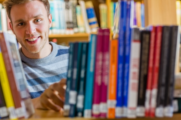 Studente maschio che seleziona libro nella biblioteca