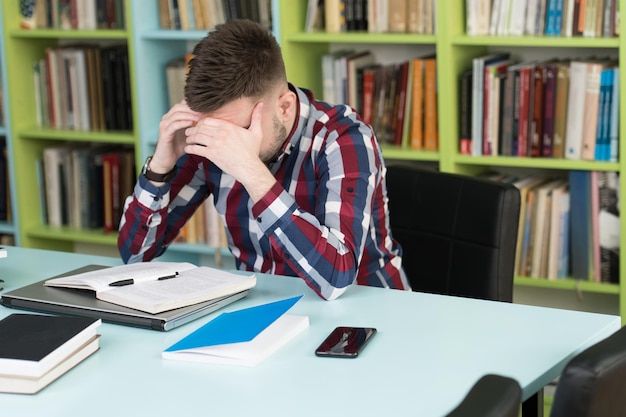 Studente maschio confuso che legge molti libri per l'esame