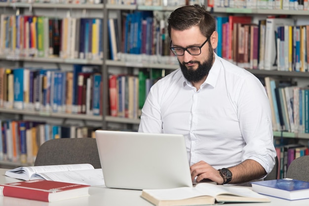 Studente maschio felice con il computer portatile in biblioteca