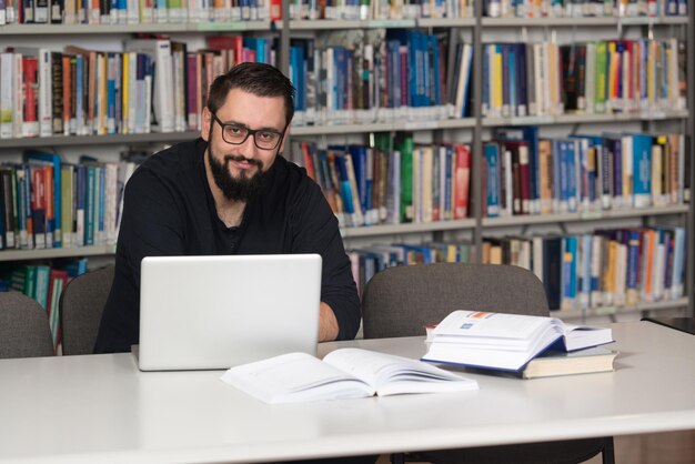 Studente maschio felice con il computer portatile in biblioteca
