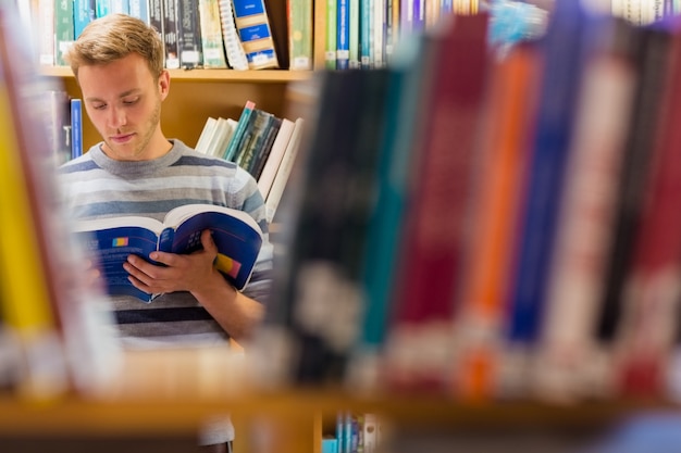 Studente maschio leggendo un libro in biblioteca