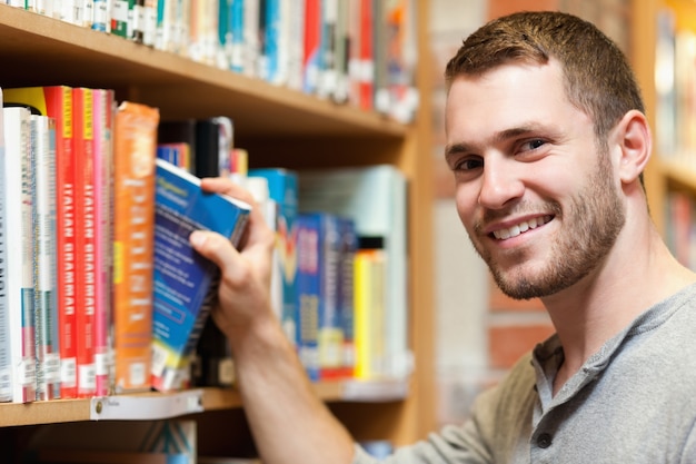 Studente maschio sorridente che seleziona un libro