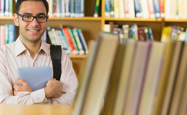 Studente maturo sorridente con il PC della compressa in biblioteca