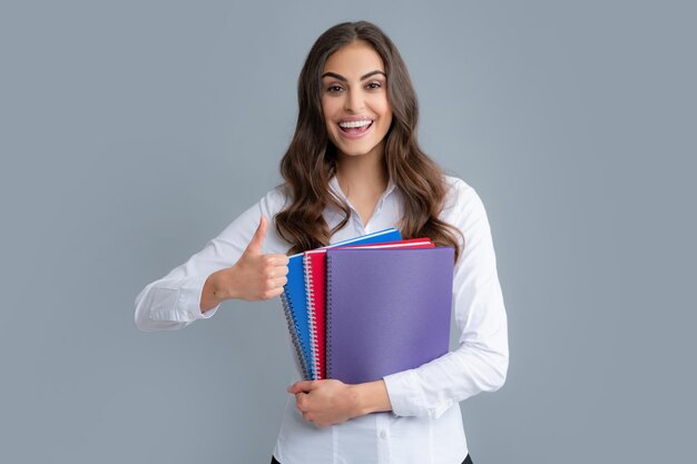 Studente o insegnante sorridente felice con i pollici in su Ragazza studentessa adolescente isolata su sfondo grigio Studentessa giovane allegra in camicia tenere quaderni Studenti universitari delle scuole superiori