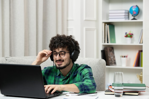 Studente online carino giovane ragazzo che studia al computer con gli occhiali in camicia verde lavorando sodo