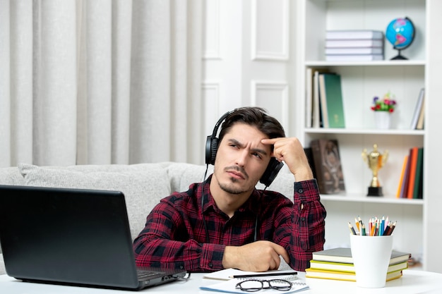 Studente online ragazzo carino in camicia a quadri con gli occhiali che studia al computer pensando e concentrato