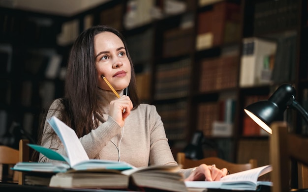 Studente pensieroso seduto intorno ai libri e pensando agli esami mentre tiene la matita