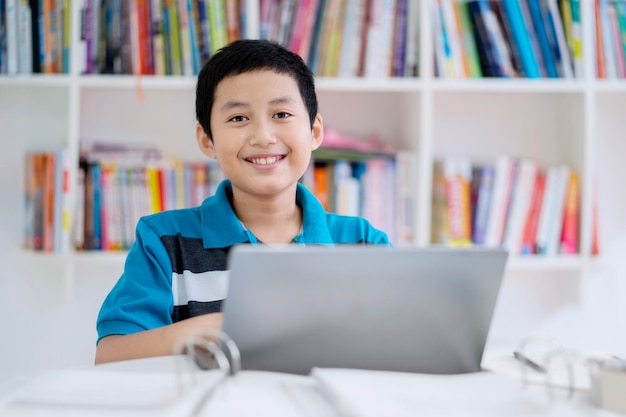 Studente preadolescente asiatico che utilizza un computer portatile in biblioteca