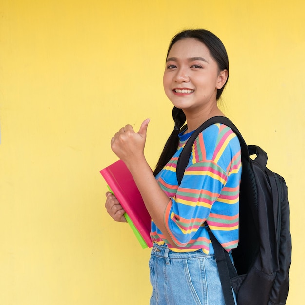 Studente ragazza tenere libro e sorridente su sfondo giallo