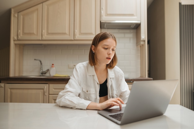 Studente seduto a una scrivania in cucina e utilizzando un computer portatile