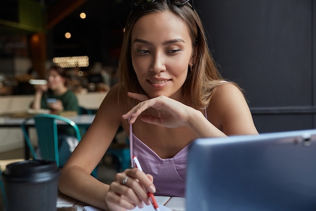 Studente seduto al tavolo della caffetteria che studia con il computer portatile che fa i compiti