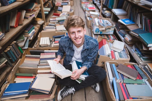 Studente seduto con i libri nelle sue mani sul pavimento in una biblioteca pubblica