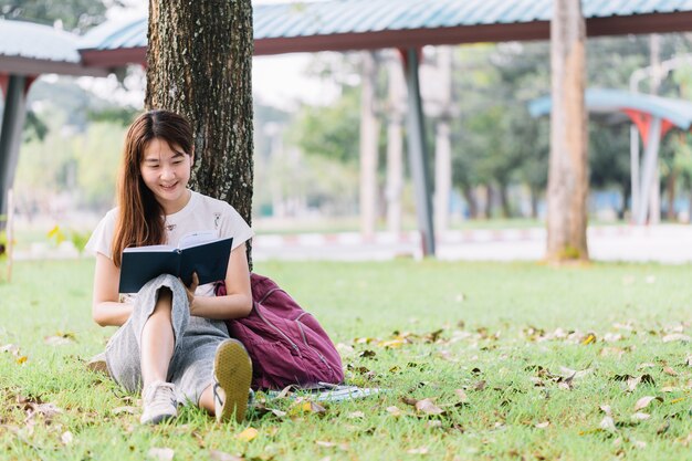 Studente seduto sotto un albero a scuola e leggendo un libro all&#39;aperto