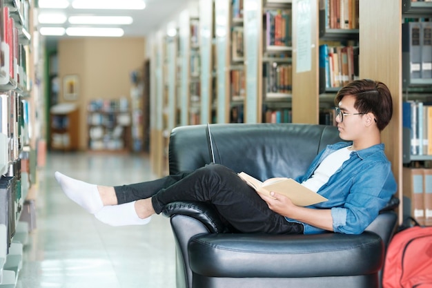 Studente seduto sul divano e che studia in biblioteca