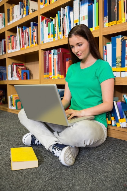 Studente seduto sul pavimento in libreria utilizzando il computer portatile