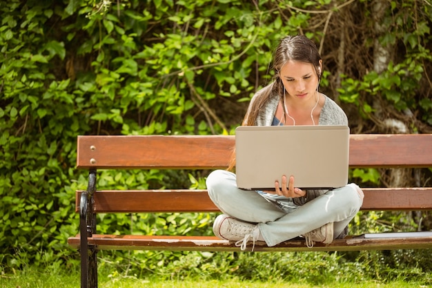 Studente seduto sulla panchina ascoltare musica e usando il portatile