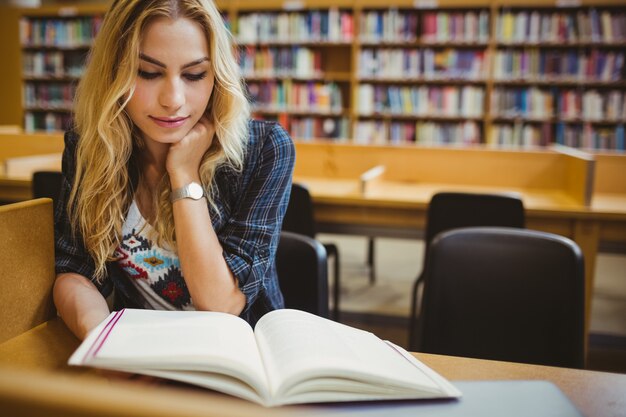 Studente sorridente che legge un libro al tavolo in biblioteca