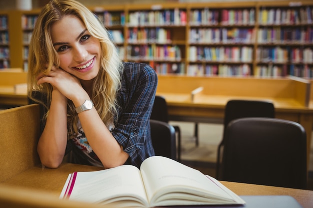 Studente sorridente che legge un libro al tavolo in biblioteca