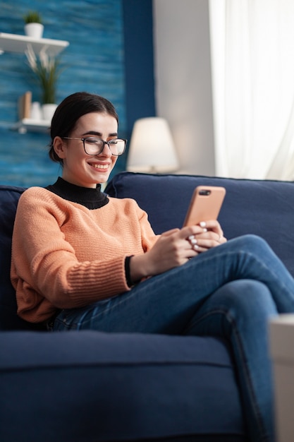 Studente sorridente che si rilassa sul divano mentre parla con i suoi amici su un messaggio sulla comunicazione sui social media. Donna adolescente che chatta sul social network utilizzando il dispositivo dell'app mobile